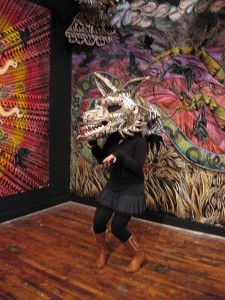A girl tries out a Dennis McNett print/papier mache wolf mask, in front of two fabulous wall-size collaged prints.