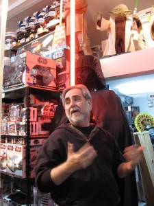 A Lego Darth Vader and boxes and boxes of stuff loom over Steve.
