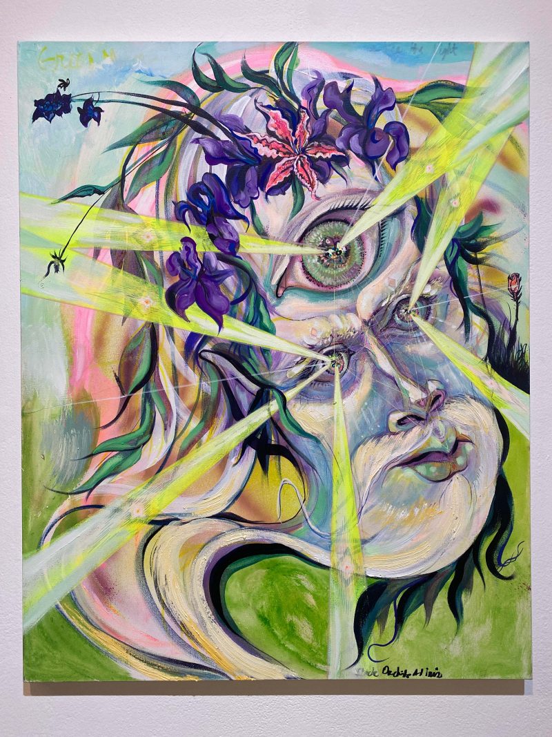 A colorful contemporary surrealist painting shows a face with three eyes and beams of light emitting from each eye.The head is festooned with purple flowers and green leaves and a flowing white beard swirls under the head.