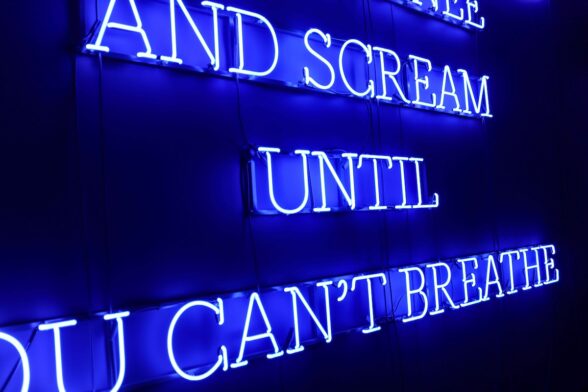 Bright blue neon letters spell out in all capitals, a message, which is partially shown here with the words, “AND SCREAM UNTIL U CAN’T BREATHE. “ The piece refers to racism in America.