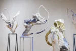 A close up of several linear and delicate-looking abstract gestural sculptures standing in a white-walled gallery space, their upward swoops suggesting a group of dancers limbering up.