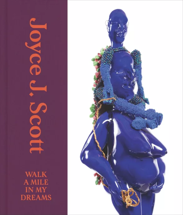 A book cover is divided vertically with the left side showing, in red letters, "Joyce J. Scott: Walk a Mile in My Dreams" and the right side showing a deep blue colored sculpture of two African figures, one sitting on the shoulders of the other. The top figure is adorned with blue beads.