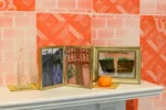 A shelf of over what might be a fireplace holds three pictures of places, which must be significant to the owners. In front of one is an orange or tomato sitting on a little mat, and to the left is a model of what might be the Eiffel Tower in glass.