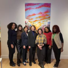 A group of women stand in front of a painting, all smiling for the camera. They are speakers at a panel about artists in Philadelphia